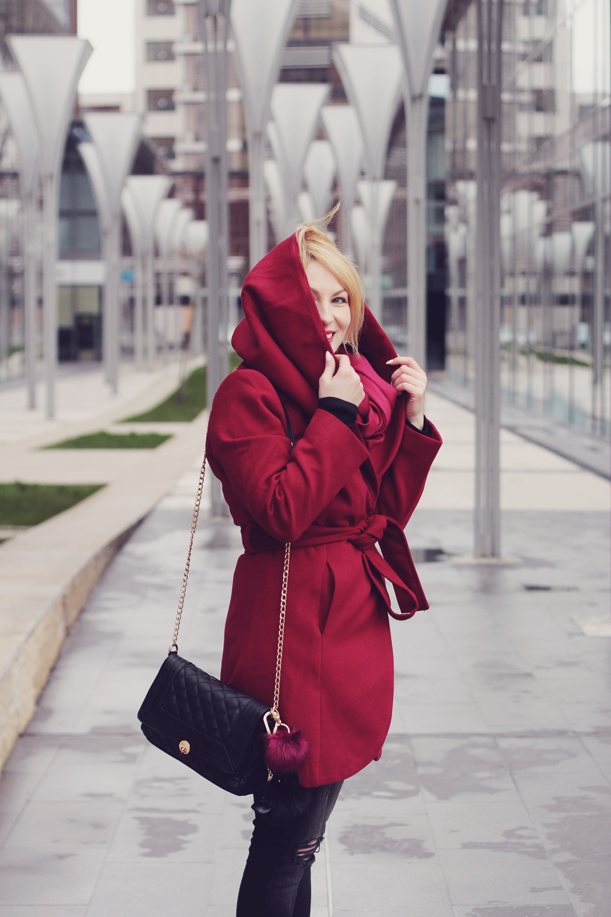burgundy coat and black chain clutch with pom-poms