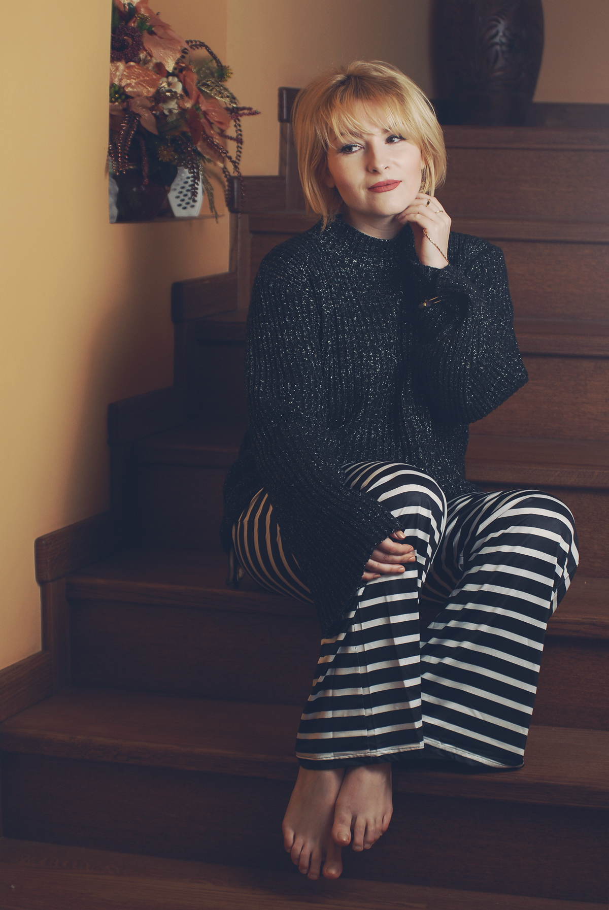 black and white striped flare pants, black sparkly sweater, matte lips, short blonde bob with bangs, lounging at home